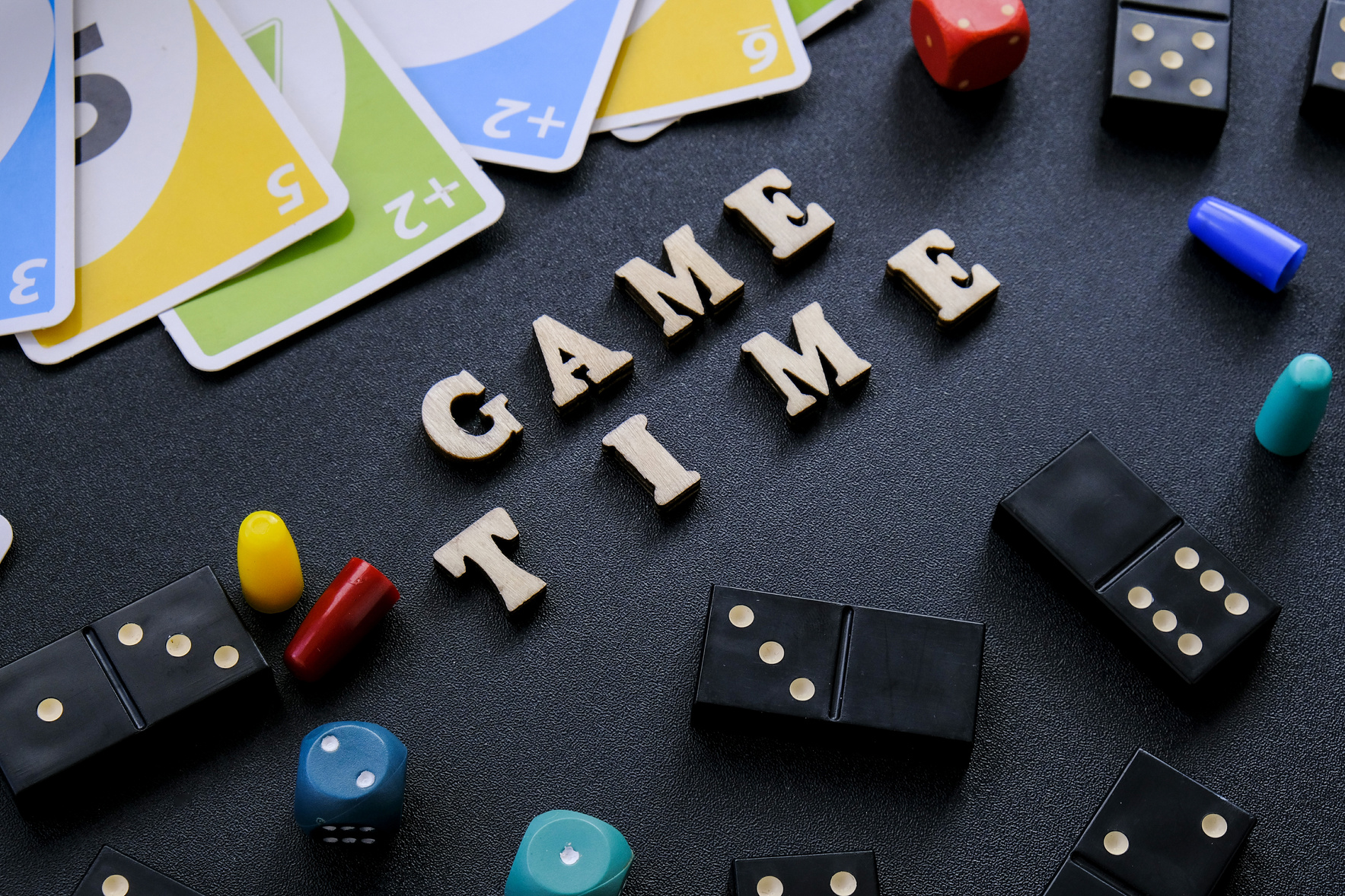 Kiev Ukraine - 10.03.21 Text GAME TIME Spelled Out in Wooden Letter. Surrounded by Dice, Dominoes Uno Playing Cards on Black Background. Table Games. Stay Home Activity